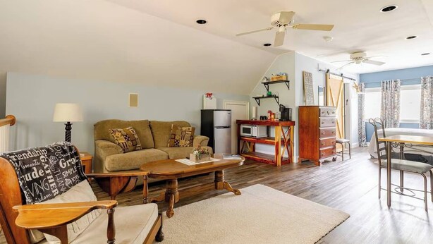 Un salon confortable avec un canapé, une table basse en bois, une table à manger avec des chaises, un coin cuisine équipé d’un four à micro-ondes et un ventilateur de plafond.