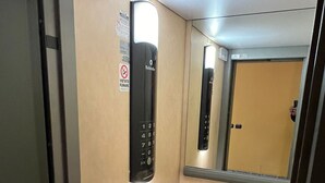 Ein schmaler Flur mit einem Wandbedienfeld für einen Aufzug und einer Tür am Ende.