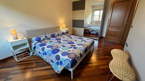 Ein Schlafzimmer mit einem Bett, Nachttischen, einem Sessel, einem Spiegel und einer Tür.