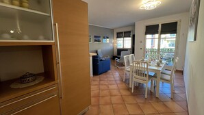 Ein Essbereich mit Tisch und Stühlen, ein blaues Sofa und eine Küchenzeile mit Schränken und einer Ablagefläche.