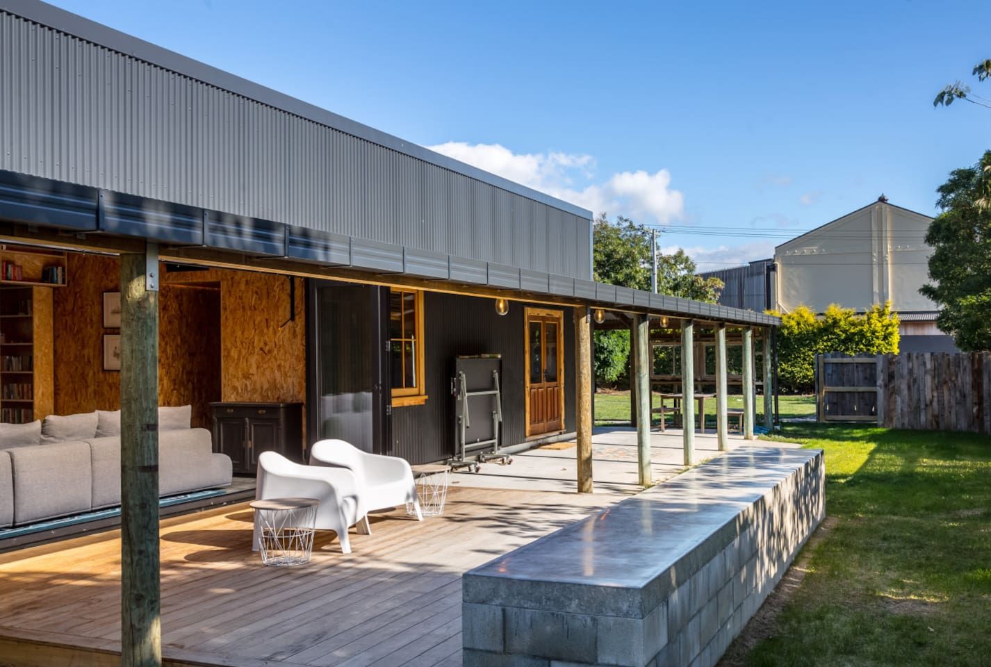 A modern outdoor patio with a wooden deck, a sofa, and white chairs.