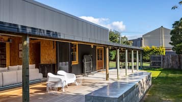 A modern outdoor patio with a wooden deck, a sofa, and white chairs.