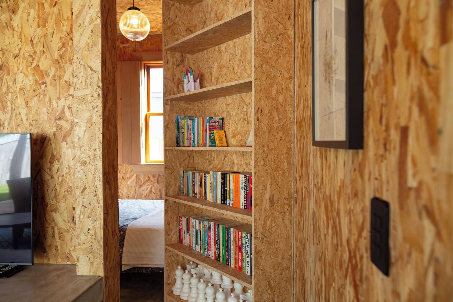 A room with a bookshelf filled with books, a television on a stand, and a bed with a blanket.