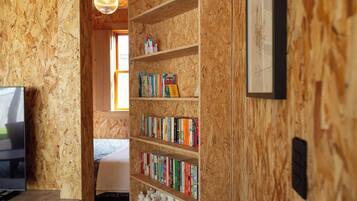 A room with a bookshelf filled with books, a television on a stand, and a bed with a blanket.