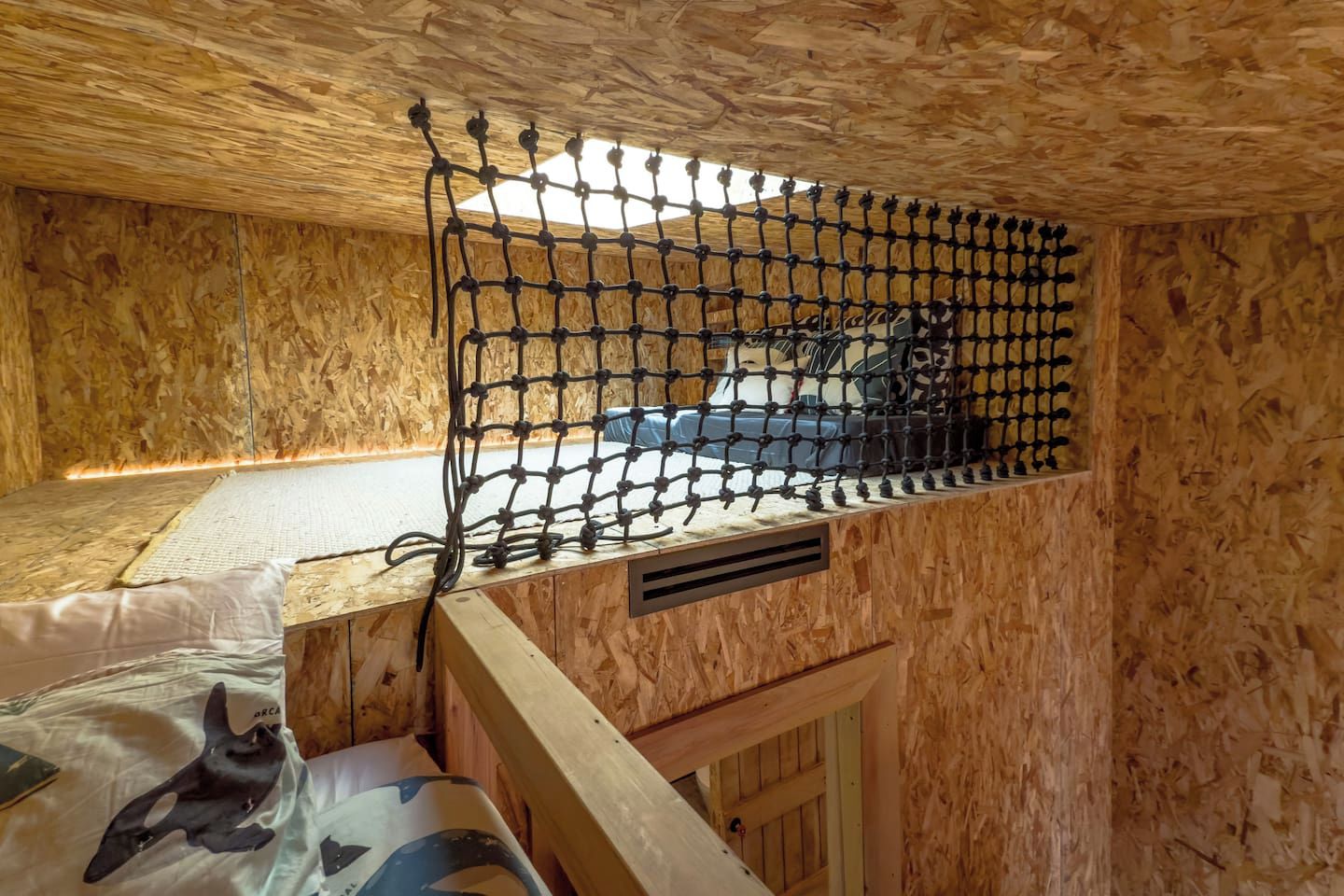 A wooden room with a bunk bed, a netted window, and a mattress with a dolphin design.