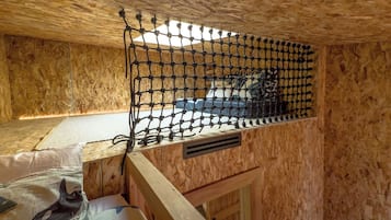 A wooden room with a bunk bed, a netted window, and a mattress with a dolphin design.