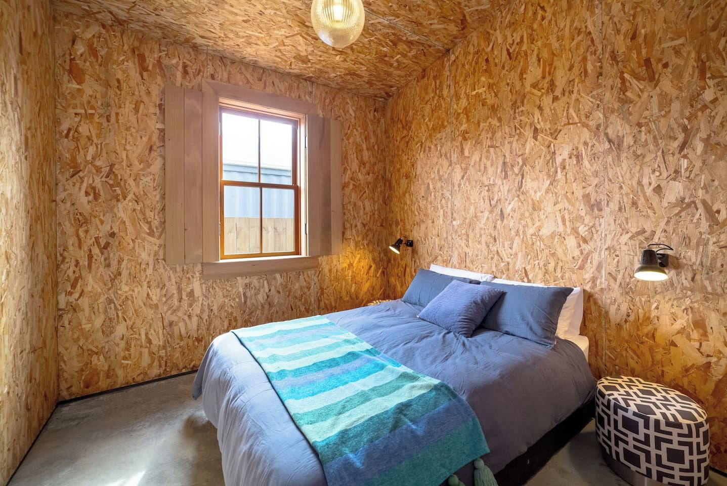 A bedroom with a bed, a window, and a wall-mounted light fixture.