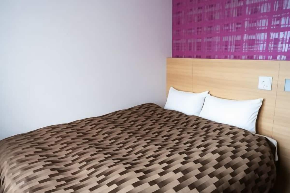 A bed with a patterned bedspread, a wooden headboard, and a pink wall.