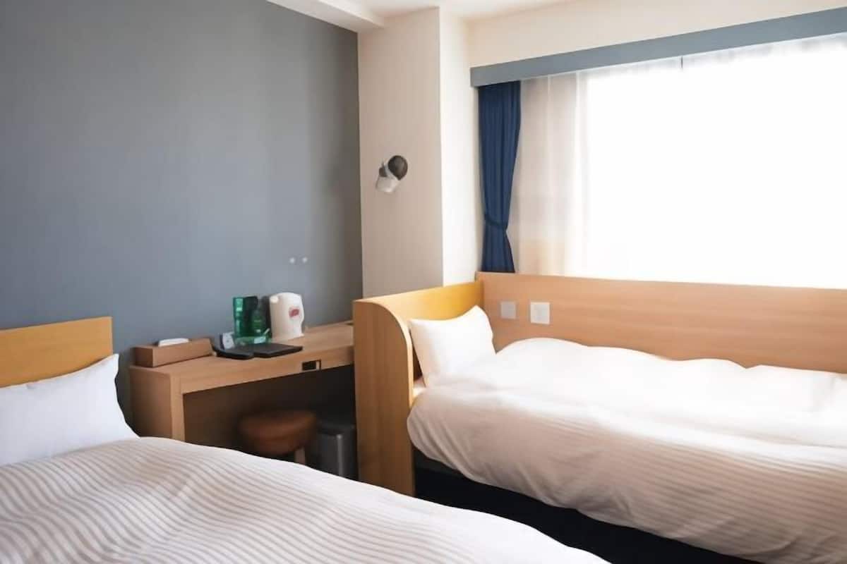 A hotel room with two beds, a desk, a chair, and a window with curtains.