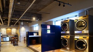 Une laverie équipée de plusieurs machines à laver, d’un appareil à café et d’un espace détente avec des tabourets.