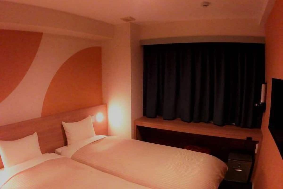 A hotel room with two beds, a flat-screen TV, and a desk with a lamp.