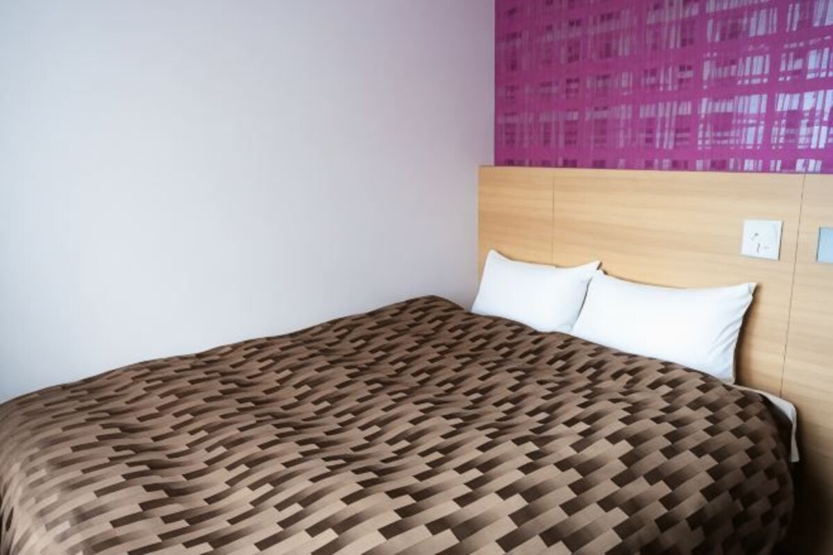 A bed with a patterned bedspread, a wooden headboard, and a pink wall.