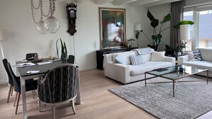 A modern living room with a dining area, featuring a large painting, a clock, and a large plant. - Sunny 3 Bedroom -Best San Francisco Neighborhood-Roofdeck w. Epic Views (San Francisco)