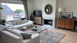 Ein modernes Wohnzimmer mit einem weißen Sofa, einem Glastisch, einem Kamin und einem Holzkabinett.