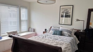 Ein Schlafzimmer mit Bett, Fensterbank, Nachttisch, Lampe und einem gerahmten Bild an der Wand.