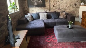 Ein Wohnzimmer mit einer Steinwand, einem Wandbild eines Stiers, einem dunkelgrauen Sofa mit vielen Kissen, einem roten Teppich mit Muster und einem Holztisch.