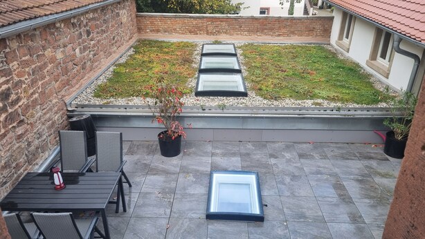 Eine Dachterrasse mit Garten, einem Tisch und Stühlen sowie einer Glastür.