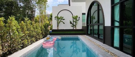Una piscina con borde de azulejos, rodeada por un muro bajo y plantas.