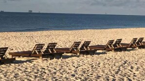 A beach with rows of wooden lounge chairs facing the ocean.