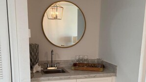 A compact kitchen with a sink, a round mirror, and a countertop with glassware.