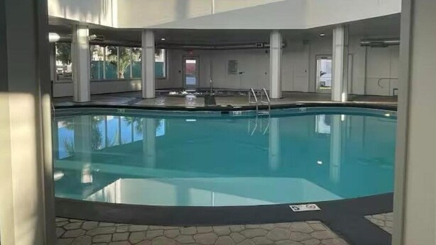 An indoor swimming pool with clear blue water, surrounded by a tiled floor and white walls.