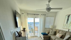 A living room with a sofa, a chair, a ceiling fan, and a view through a glass door to the outside.
