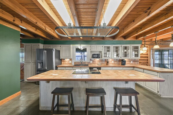 A spacious kitchen with a large island, wooden ceiling beams, and bar stools. - The Aledo Prospector (Aledo)