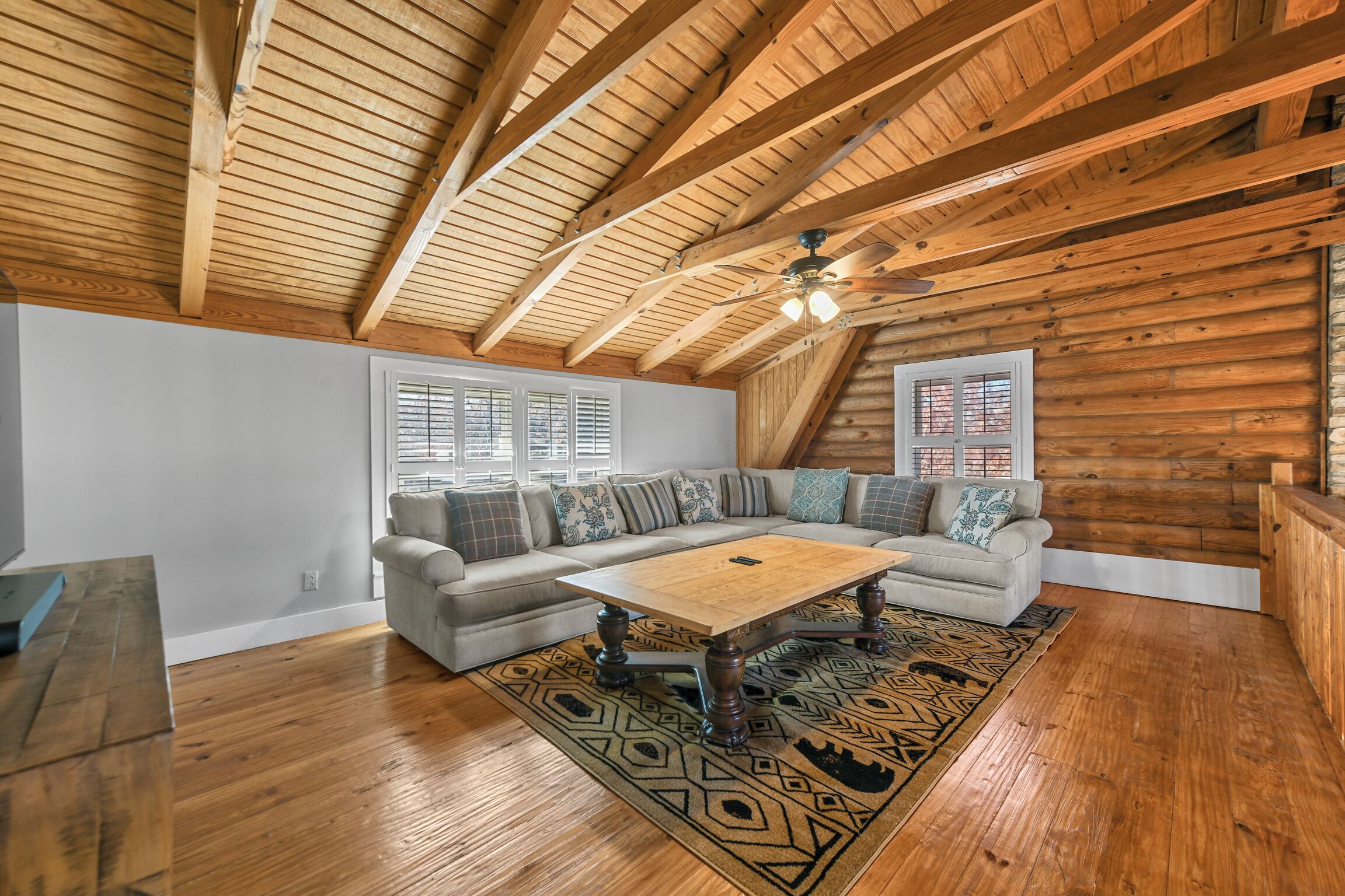 Un loft espacioso con un alto techo de madera, un amplio sofá modular, una mesa de centro de madera y una alfombra estampada.