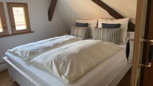 A bedroom with a sloped ceiling, a wooden beam structure, a double bed with white bedding, striped pillows, and a wooden door. - Schmuckstück Maikammer - unique atmosphere with that certain something Whg. 5 (Maikammer)