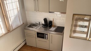 A compact kitchen with a sink, stove, and microwave. There is a window with curtains, a framed picture on the wall, and a small rug on the floor. - Schmuckstück Maikammer - unique atmosphere with that certain something Whg. 5 (Maikammer)