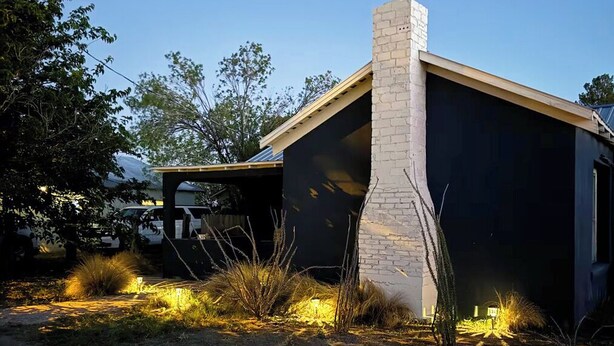 A modern house with a large chimney, a garage, and a well-lit garden area. - La Casita Azul - Cozy Casita with Large Backyard in Marfa, TX (Marfa)