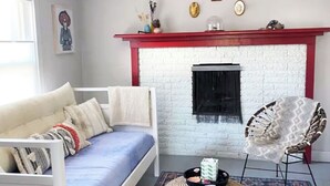 A cozy room with a white bed, a red fireplace, and a patterned chair. - La Casita Azul - Cozy Casita with Large Backyard in Marfa, TX (Marfa)