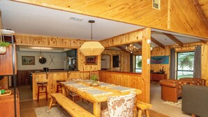 A wooden interior with a dining table, benches, a sofa, and a kitchen area.