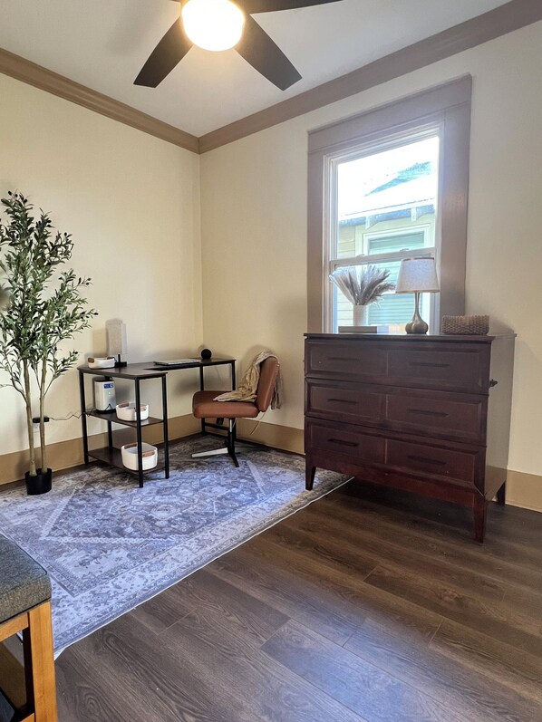 Una habitación con escritorio, silla, cómoda y una planta en maceta.