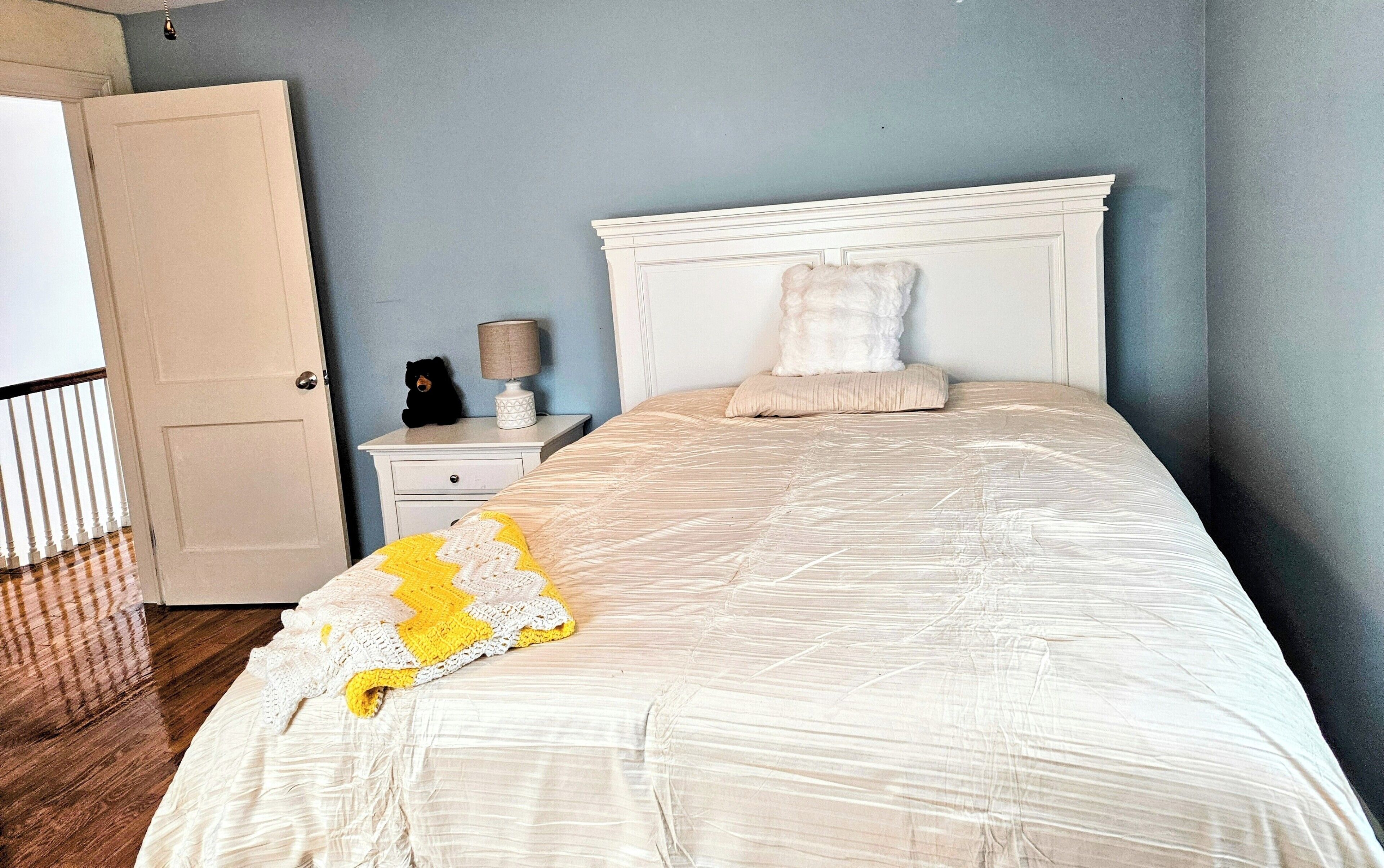 A bedroom with a bed, a nightstand, a lamp, a teddy bear, and a door.