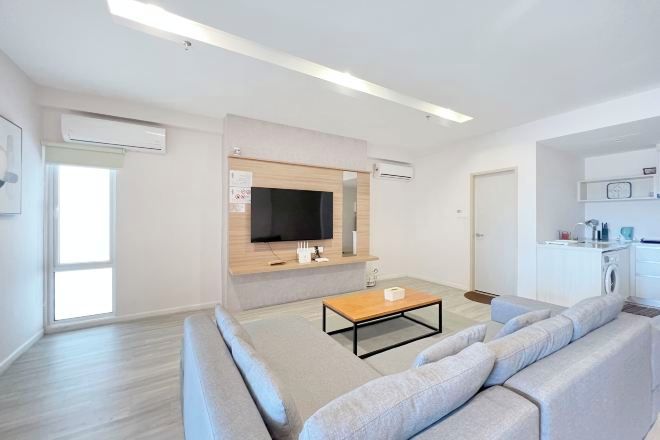 Un salon moderne comprenant un canapé, une table basse, un téléviseur fixé au mur et un coin cuisine avec un lave-linge.