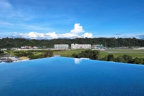 A hotel with a rooftop pool overlooking a cityscape, including buildings and a forested area. - Restful Respite Tanjung Aru Inifnity Pool 2BR (Kota Kinabalu)