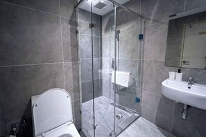 Ein modernes Badezimmer mit einer Glaskabine, einer weißen Toilette und einem Waschbecken mit Spiegel.