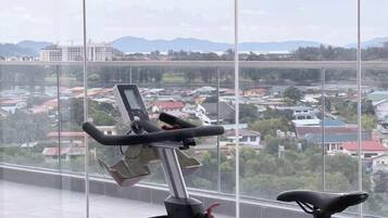 A stationary bike with a digital display, positioned in a room with large windows overlooking a residential area.