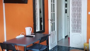 Ein Zimmer mit Tisch, Stühlen, einem Fernseher und einer Tür zu einem weiteren Raum.
