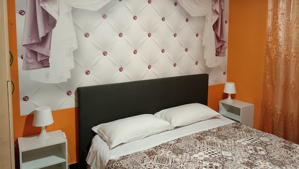 Ein Schlafzimmer mit einer gepolsterten Kopfteil, weißer Bettwäsche, einem gemusterten Überwurf und zwei Nachttischen mit Lampen.