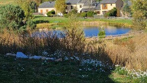 A rural landscape with a pond, a small building, and a forested hill in the background.
