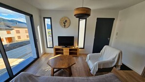A modern living room with a large window, a wooden table, a TV, and a cozy seating area.