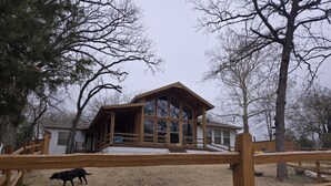 Eine Holzhütte mit großer Glasfront, einer Holzdiele und einem eingezäunten Garten.