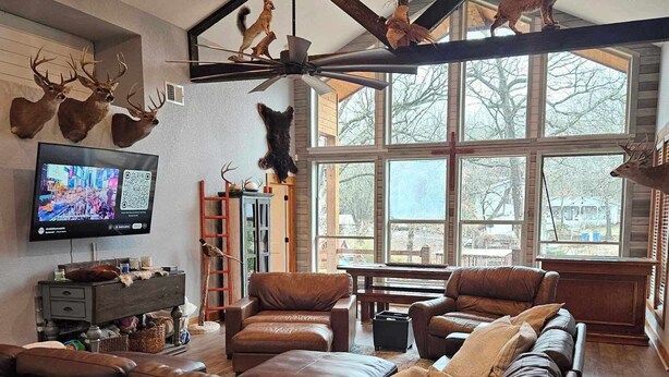 Ein geräumiges Wohnzimmer mit einem großen Ecksofa, einem an der Wand montierten Fernseher und einem Deckenventilator.