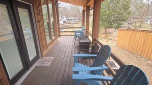 Eine überdachte Terrasse mit Holzboden und Deckenventilator, mit blauen Adirondack-Stühlen und einem Holzzaun im Hintergrund.