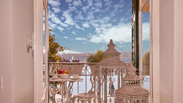 A balcony with ornate metal railings, a small table with cups and a bowl of fruit, and a view of a mountainous landscape. - Romantic Benaco Sal - App 01 (Salò)