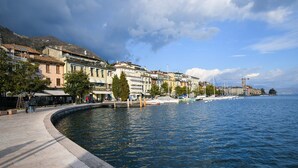 A waterfront promenade with buildings, a curved pathway, and a calm sea. - Romantic Benaco Sal - App 01 (Salò)