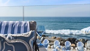 A beachside view with a glass of white wine, striped towels, and beach chairs.