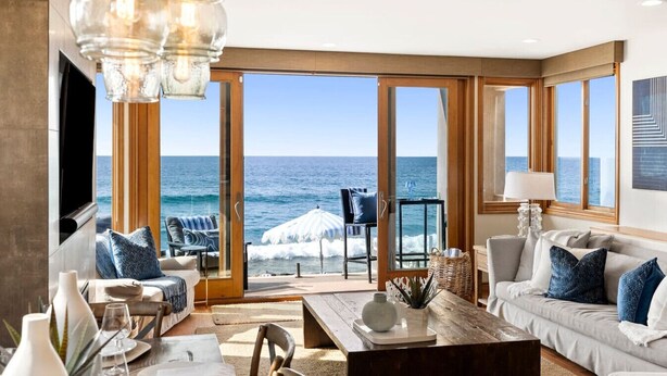 A spacious living room with a large glass door leading to a balcony overlooking the ocean.